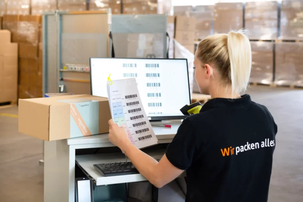 Effiziente Überprüfung des Abwicklungsprozesses von Waren Mitarbeiterin überprüft Versandetiketten und Pakete am Computerarbeitsplatz im Fulfillment-Lager