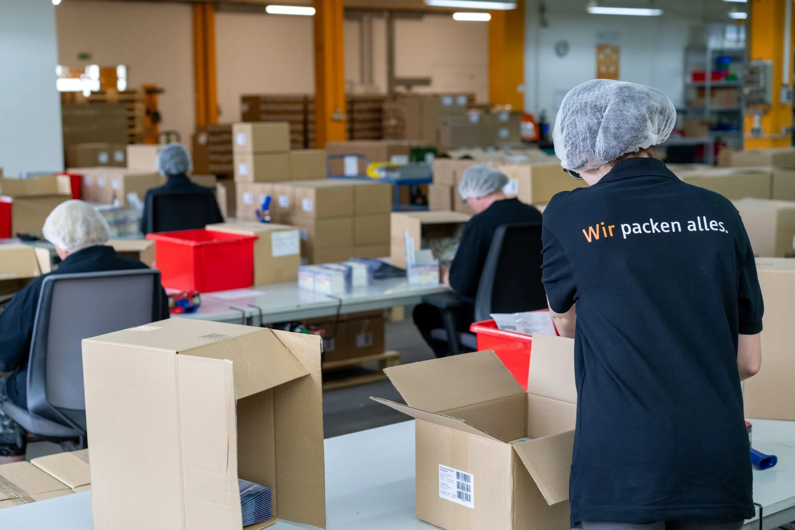 Wir packen alles: Teamarbeit am Packtisch Mitarbeiter verpacken Produkte gemeinsam an Packtischen in einer Verpackungsproduktion